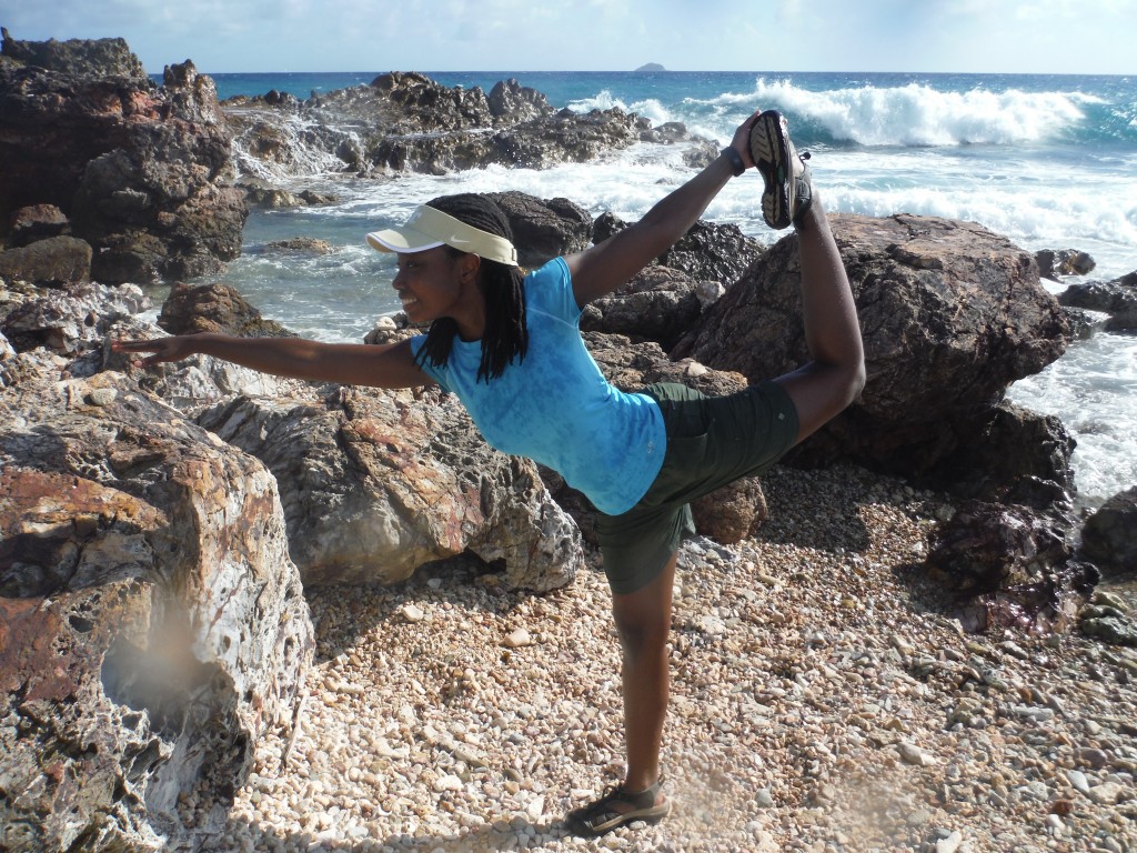 black woman with dreadlocks doing yoga poses at the beach